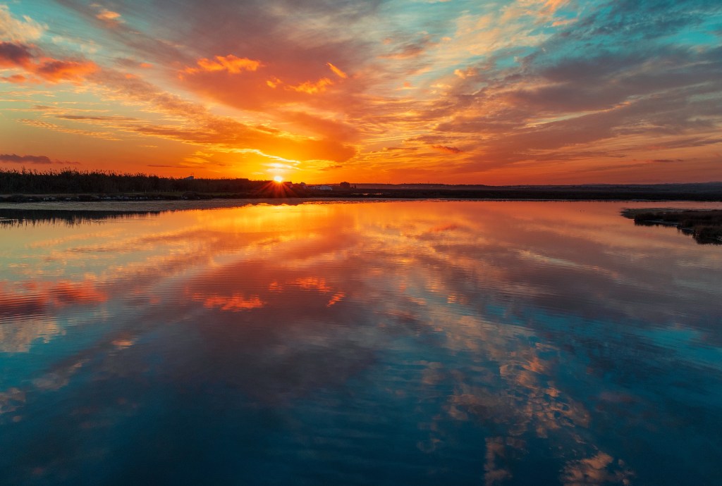 red sunset on horizon over blue sea, red mirrored in sea